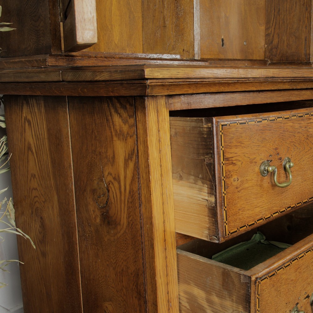 A solid honey-coloured oak dresser featuring a top section with open shelving and small side cupboards, set upon a base with six drawers and brass swan-neck handles. View XI