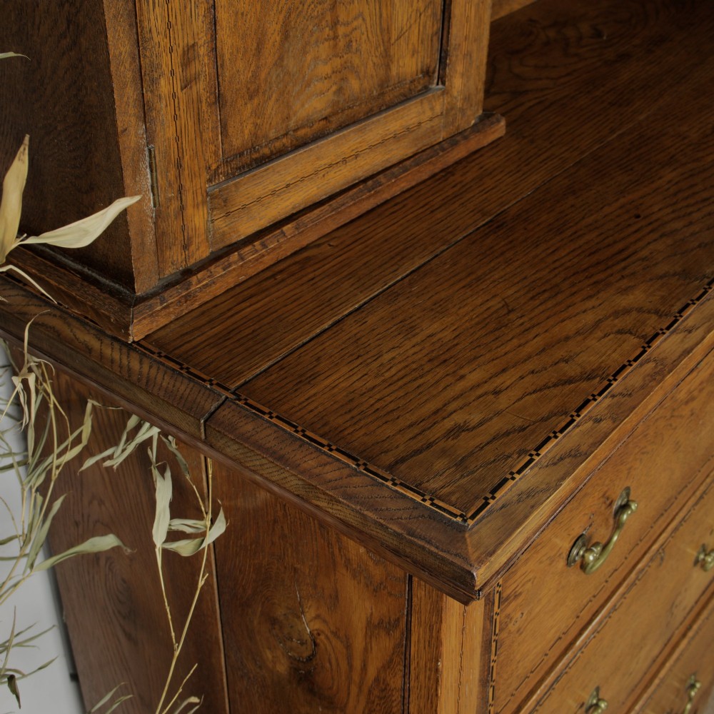 A solid honey-coloured oak dresser featuring a top section with open shelving and small side cupboards, set upon a base with six drawers and brass swan-neck handles. View XII