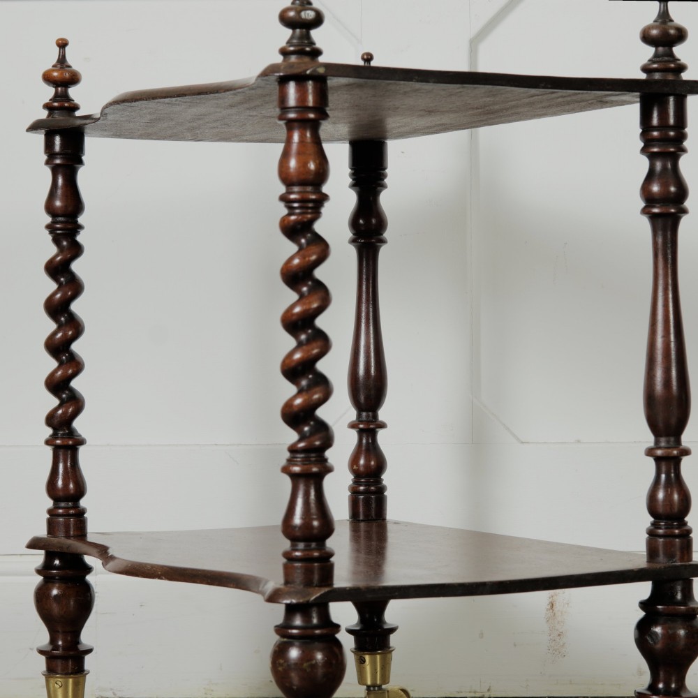 A dark wood Victorian two-tier whatnot featuring hand-turned barley twist legs, top corner finials, and brass casters. View V