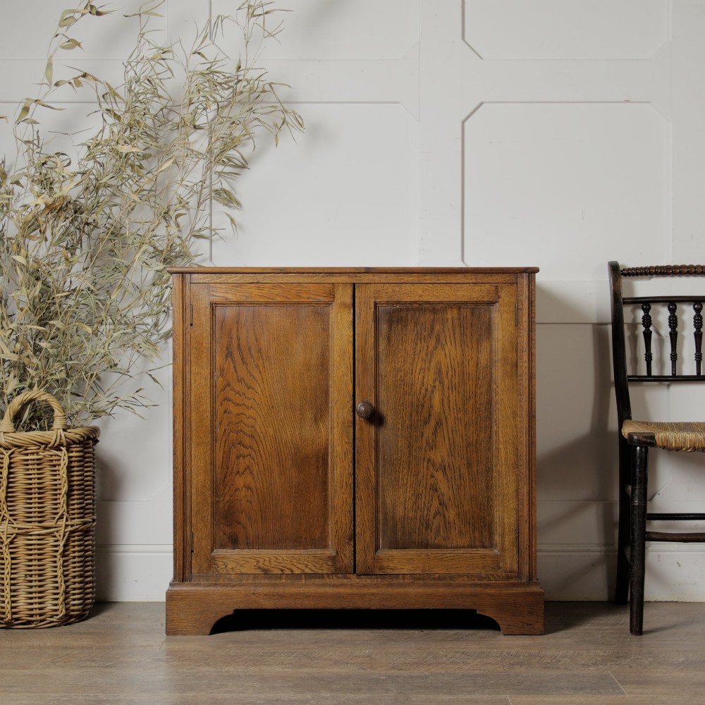 A solid oak low cupboard featuring two panelled doors with a central wooden knob handle set on a shaped plinth base.