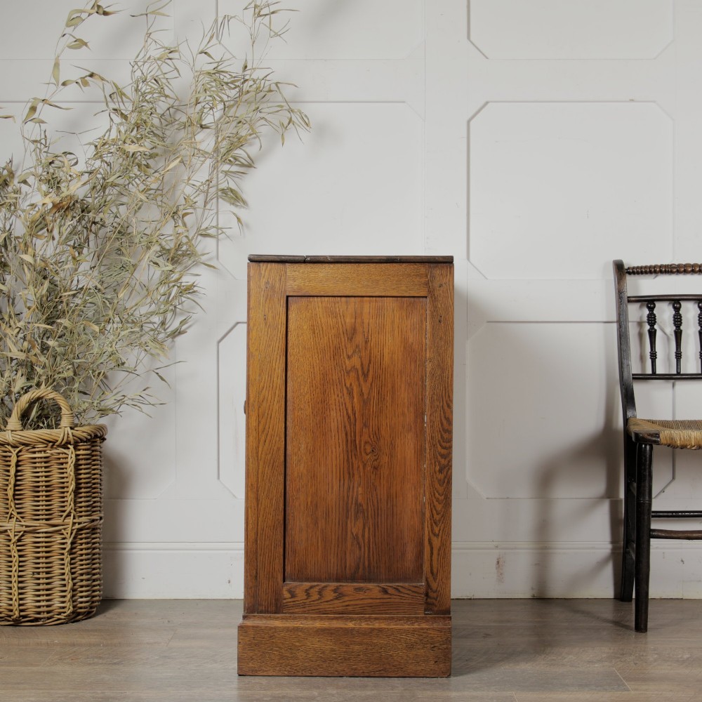 A solid oak low cupboard featuring two panelled doors with a central wooden knob handle set on a shaped plinth base. View III