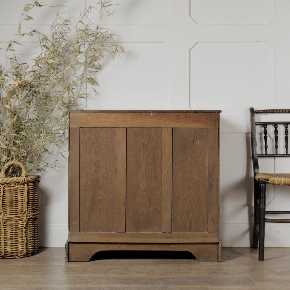 A solid oak low cupboard featuring two panelled doors with a central wooden knob handle set on a shaped plinth base. View IV