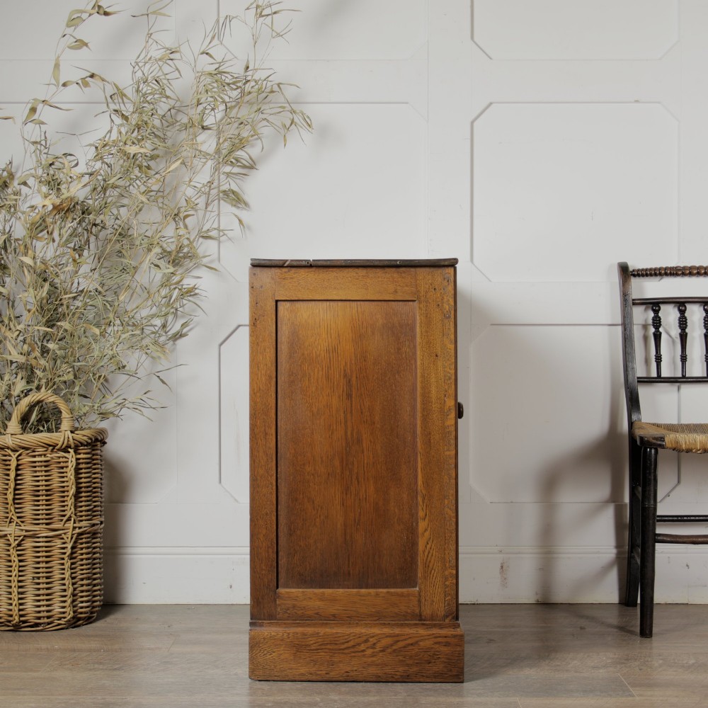 A solid oak low cupboard featuring two panelled doors with a central wooden knob handle set on a shaped plinth base. View V