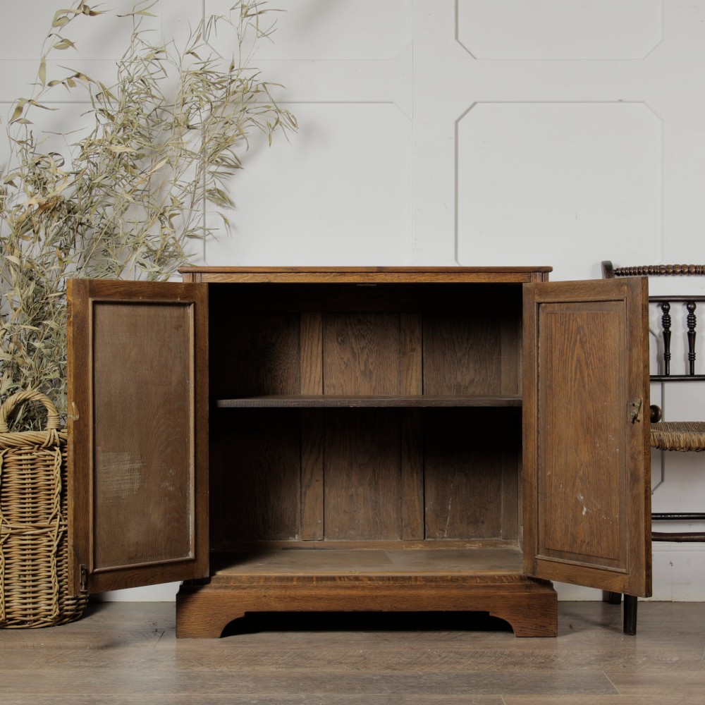 A solid oak low cupboard featuring two panelled doors with a central wooden knob handle set on a shaped plinth base. View VI