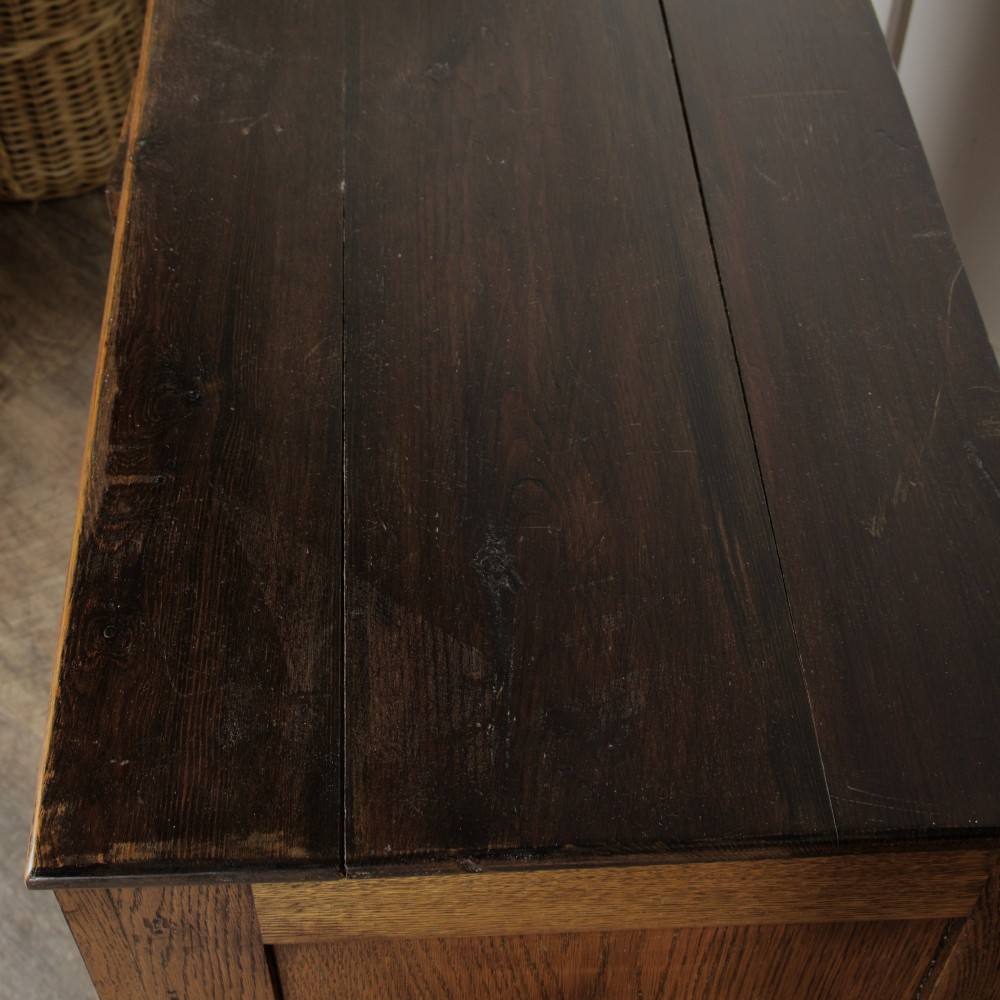 A solid oak low cupboard featuring two panelled doors with a central wooden knob handle set on a shaped plinth base. View VIII