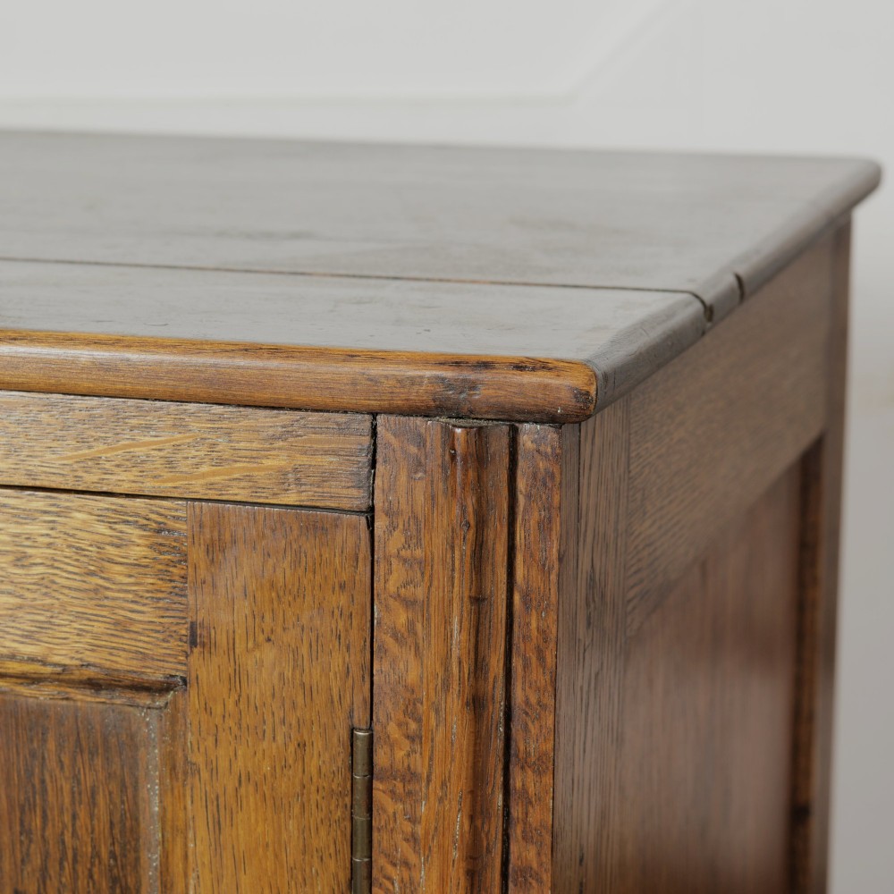 A solid oak low cupboard featuring two panelled doors with a central wooden knob handle set on a shaped plinth base. View IX