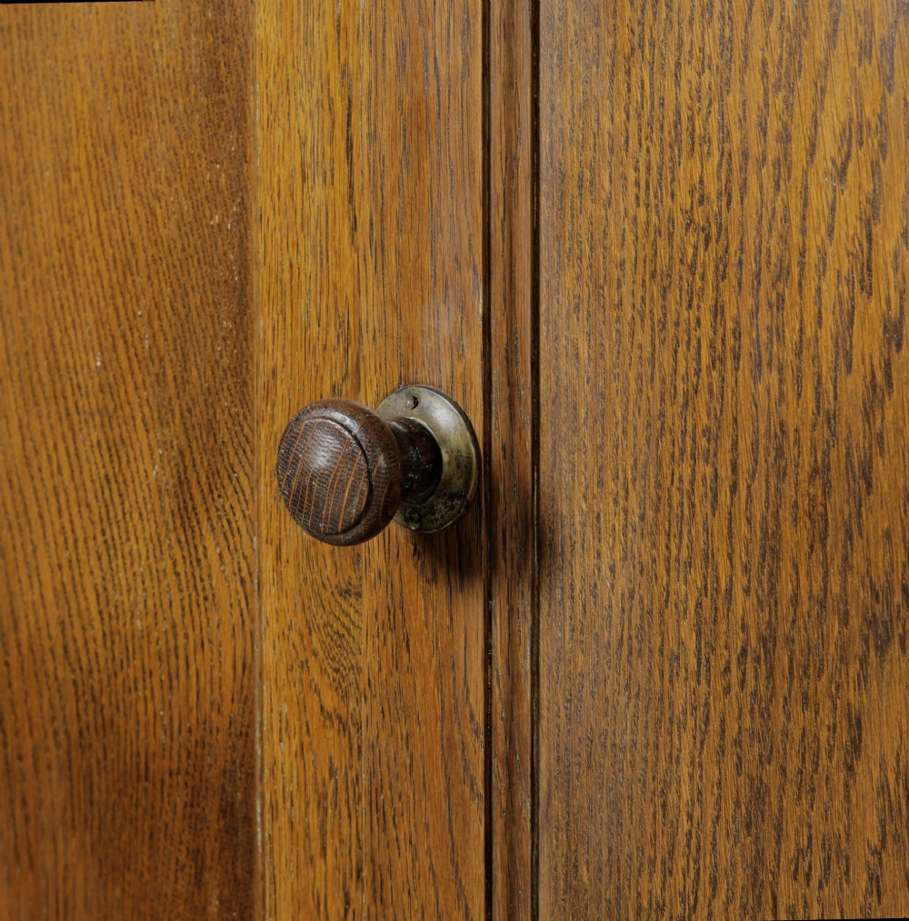 A solid oak low cupboard featuring two panelled doors with a central wooden knob handle set on a shaped plinth base. View X