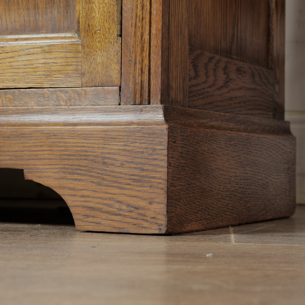 A solid oak low cupboard featuring two panelled doors with a central wooden knob handle set on a shaped plinth base. View XI