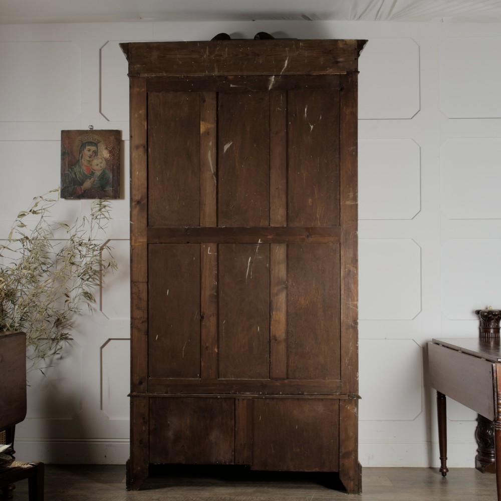 An early 20th-century satinwood wardrobe featuring a central mirrored door, carved top pediment, panelled sides, and a single lower drawer with metal drop handles. View II