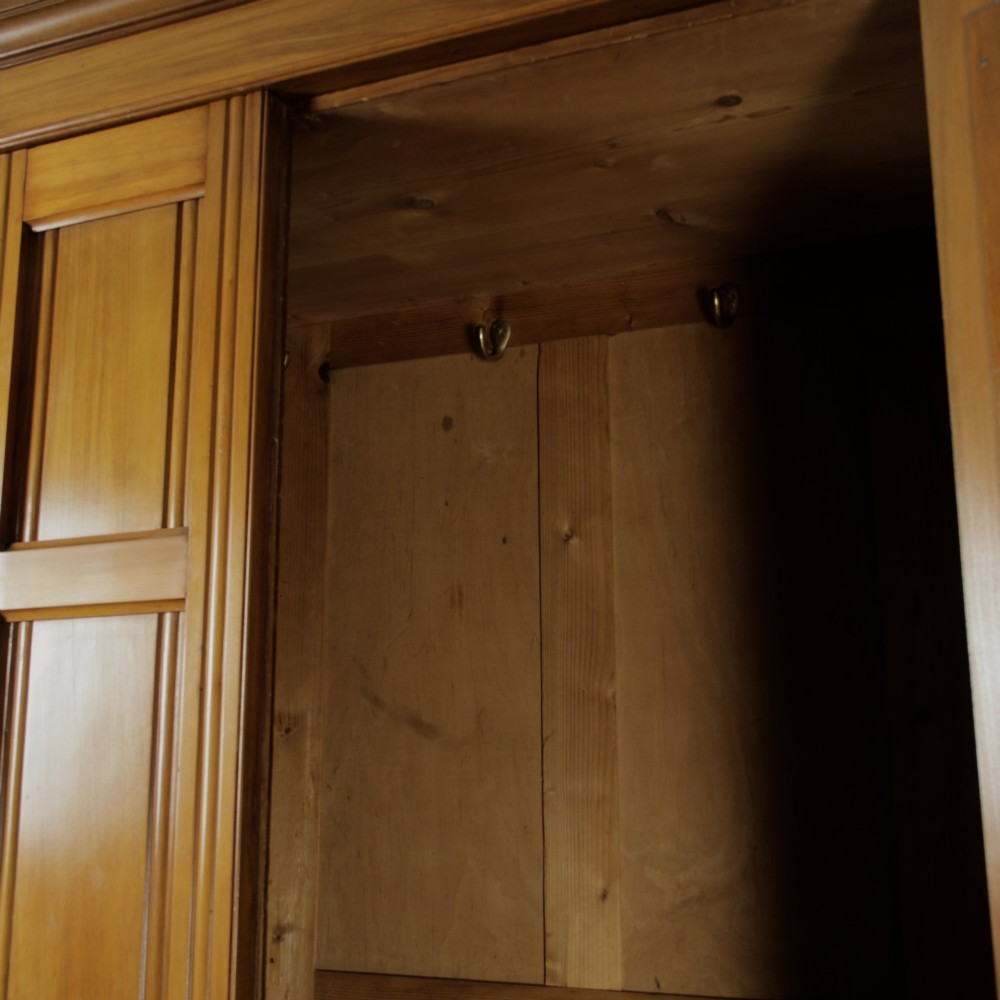 An early 20th-century satinwood wardrobe featuring a central mirrored door, carved top pediment, panelled sides, and a single lower drawer with metal drop handles. View V