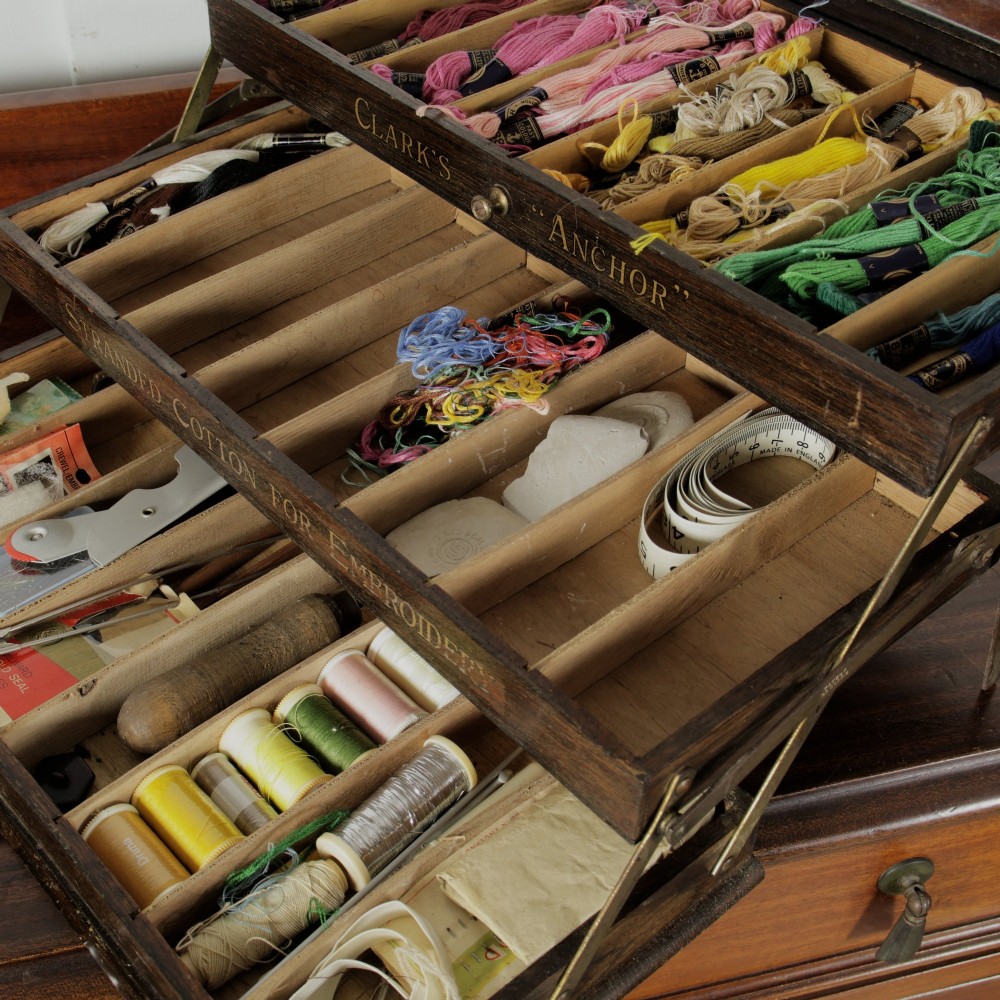 A dark wooden multi-tiered cantilever haberdashery display box with a glass lid bearing a yellow anchor logo, shown open with thread spools inside. View VIII