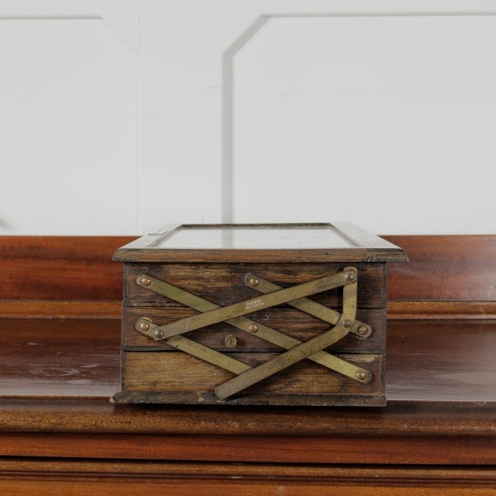 A dark wooden multi-tiered cantilever haberdashery display box with a glass lid bearing a yellow anchor logo, shown open with thread spools inside. View XI