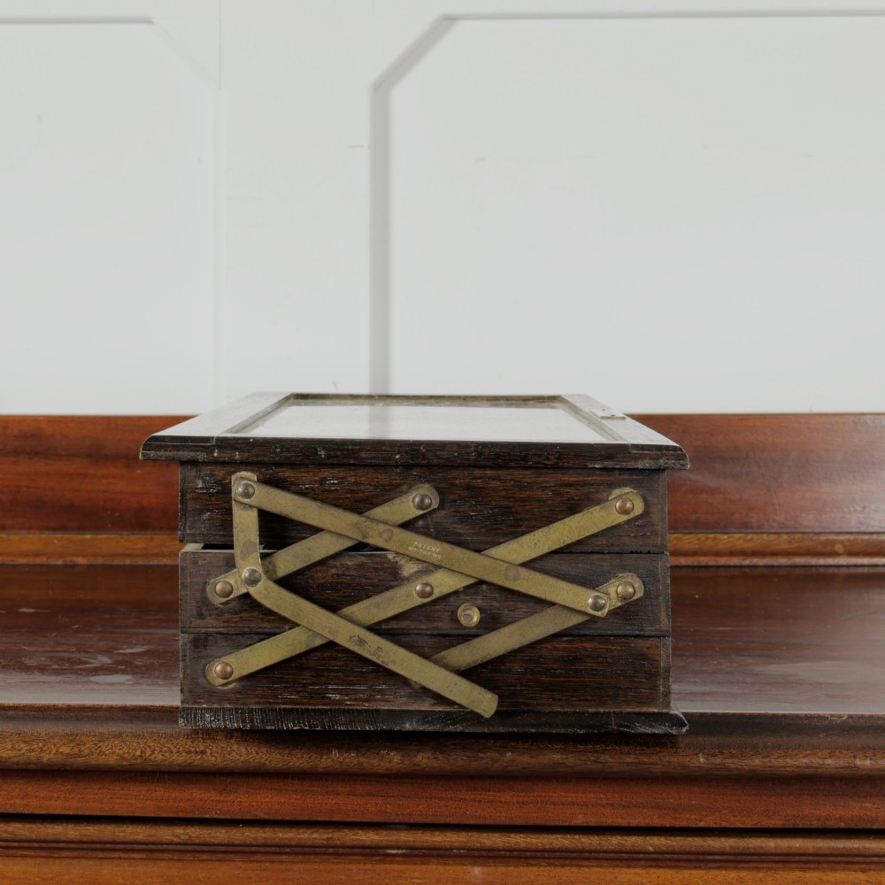 A dark wooden multi-tiered cantilever haberdashery display box with a glass lid bearing a yellow anchor logo, shown open with thread spools inside. View XIII