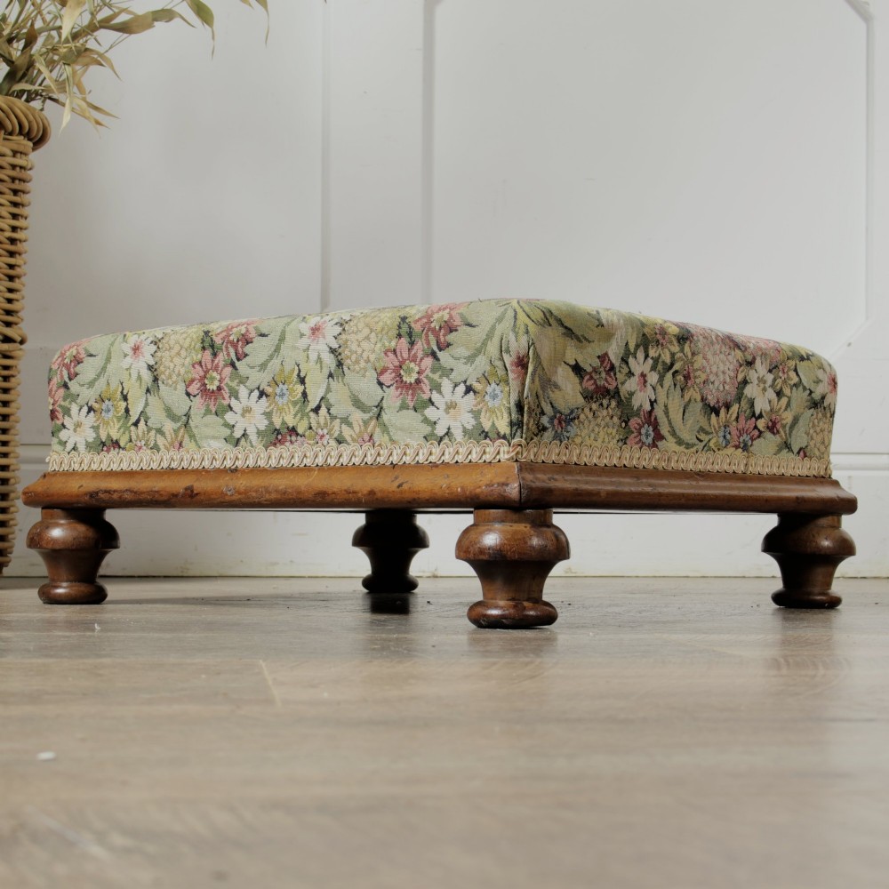 A low Victorian square footstool with green floral tapestry upholstery, decorative braid trim, and turned mahogany feet. View II