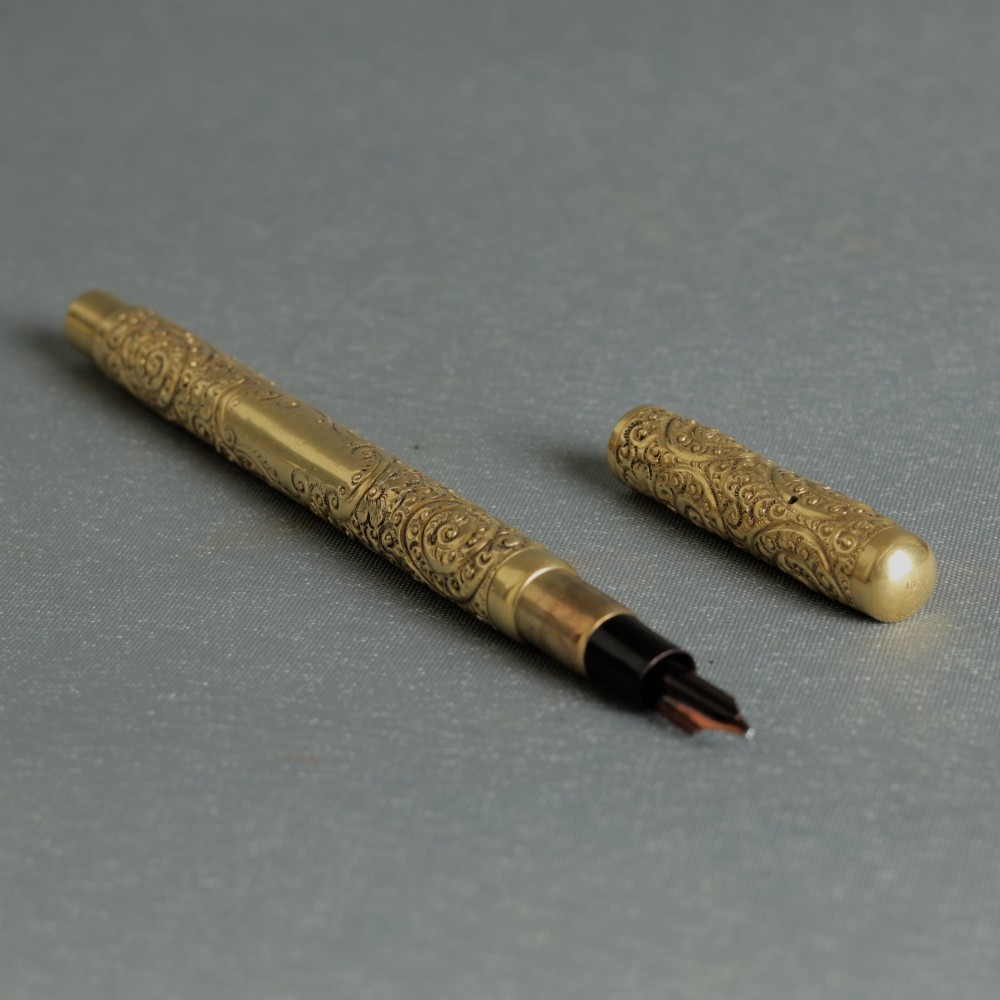 An antique Mabie Todd Swan fountain pen with a detailed chased rolled gold barrel, unscrewed cap, and dark ebonite section with exposed nib.