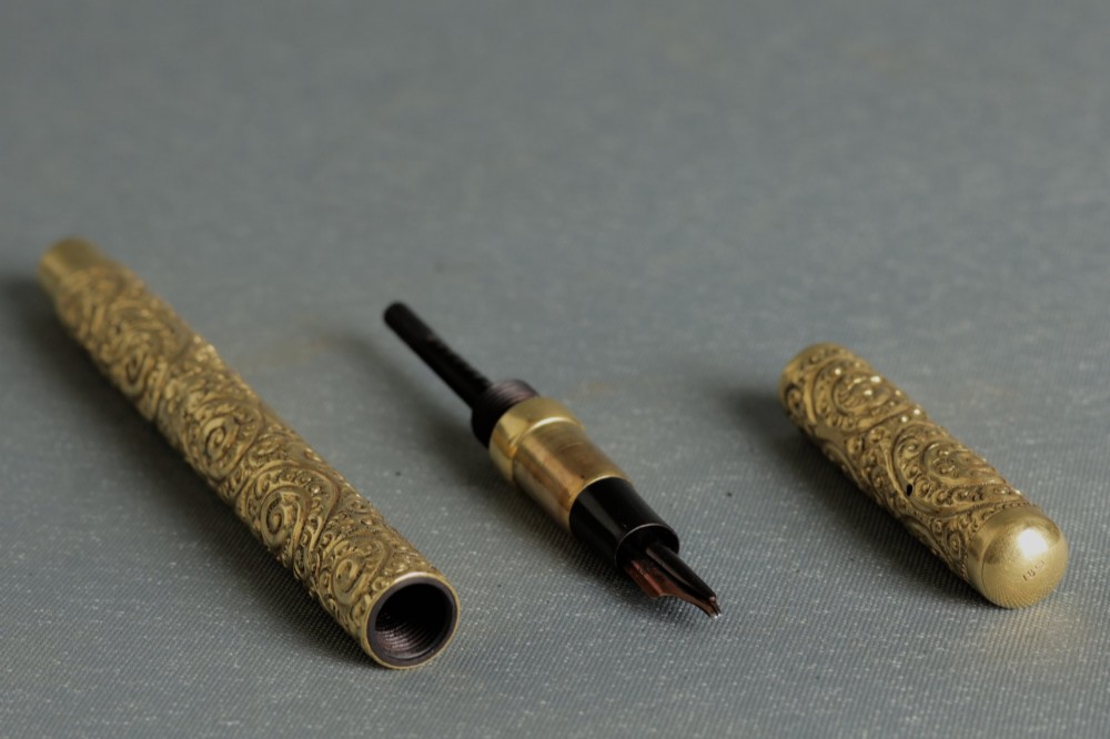 An antique Mabie Todd Swan fountain pen with a detailed chased rolled gold barrel, unscrewed cap, and dark ebonite section with exposed nib. View III