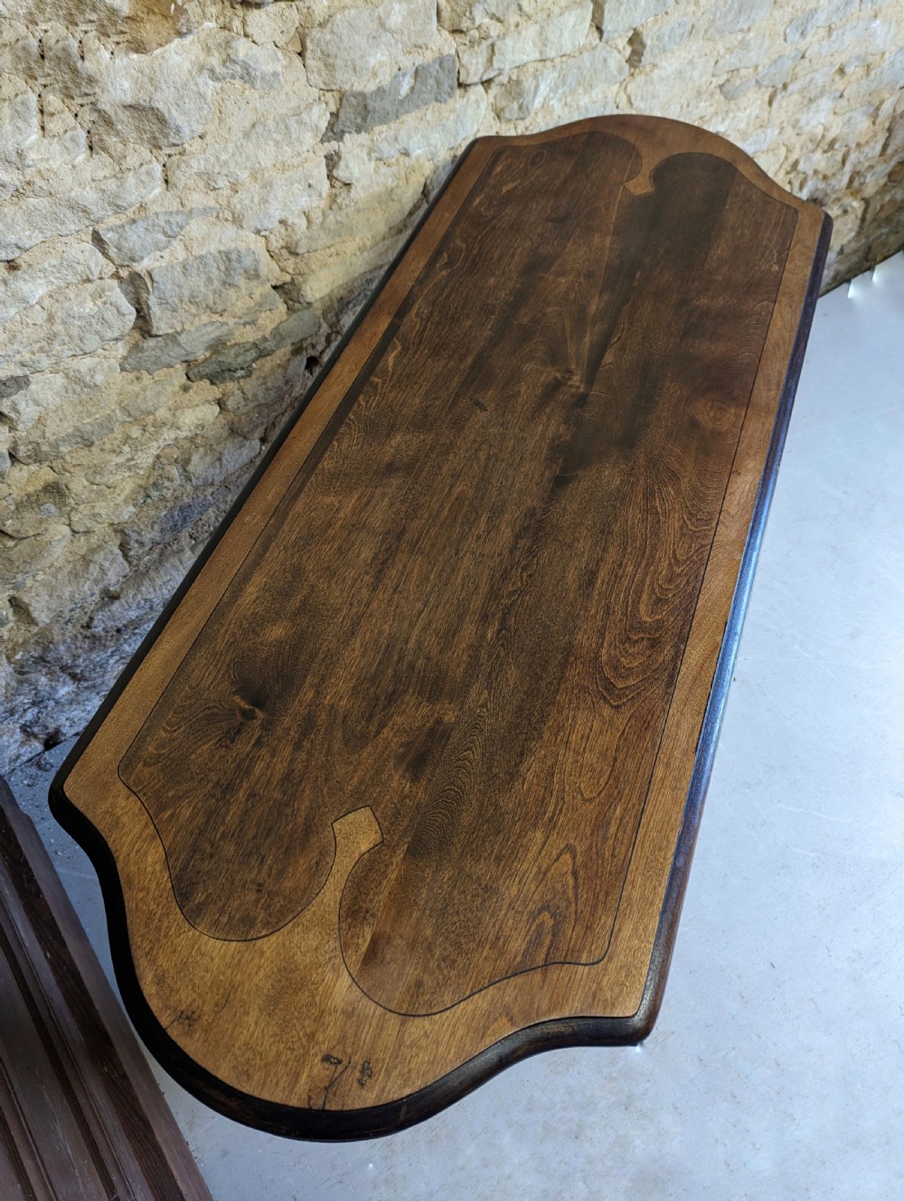 A late 19th-century dark oak trestle table featuring a shaped top with contrasting inlaid border and a low stretcher with a central carved boss. View III