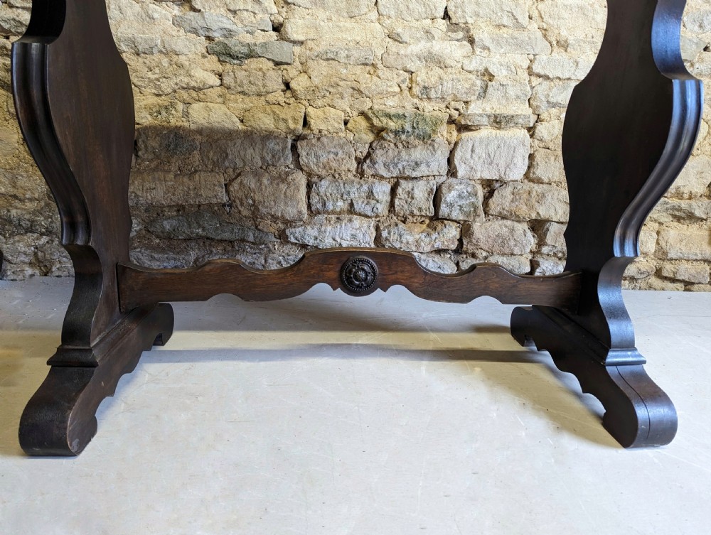 A late 19th-century dark oak trestle table featuring a shaped top with contrasting inlaid border and a low stretcher with a central carved boss. View V