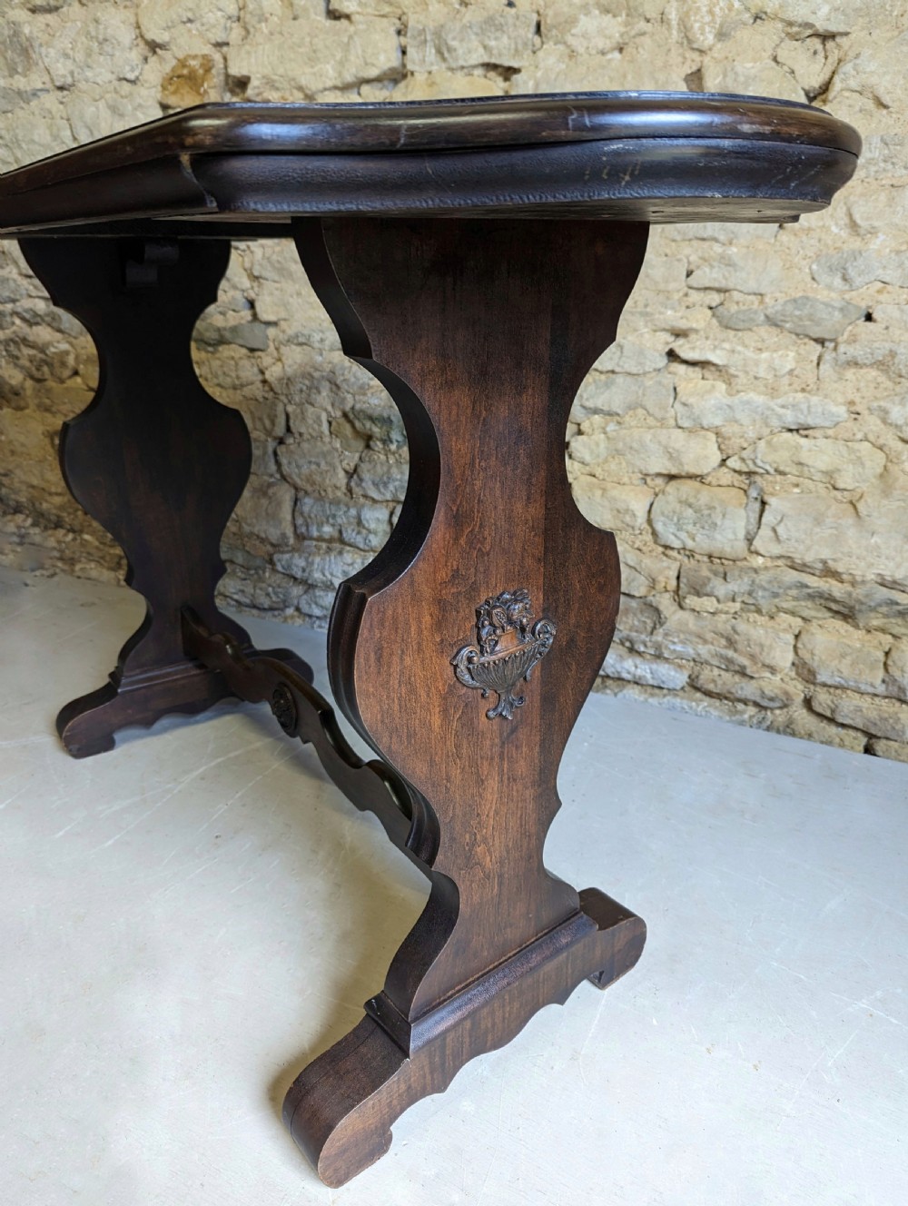 A late 19th-century dark oak trestle table featuring a shaped top with contrasting inlaid border and a low stretcher with a central carved boss. View VII