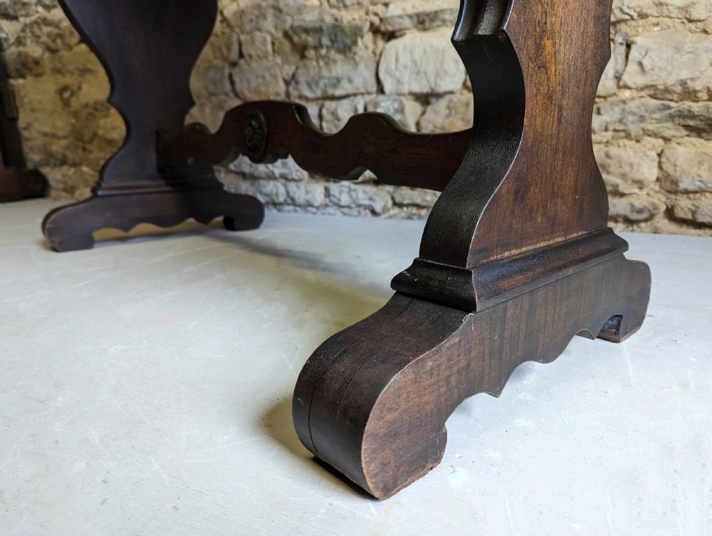 A late 19th-century dark oak trestle table featuring a shaped top with contrasting inlaid border and a low stretcher with a central carved boss. View VIII