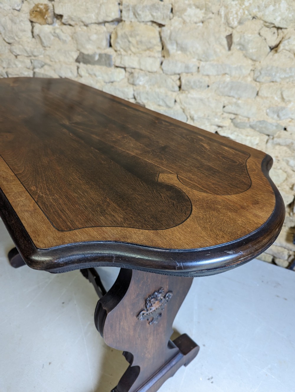 A late 19th-century dark oak trestle table featuring a shaped top with contrasting inlaid border and a low stretcher with a central carved boss. View X
