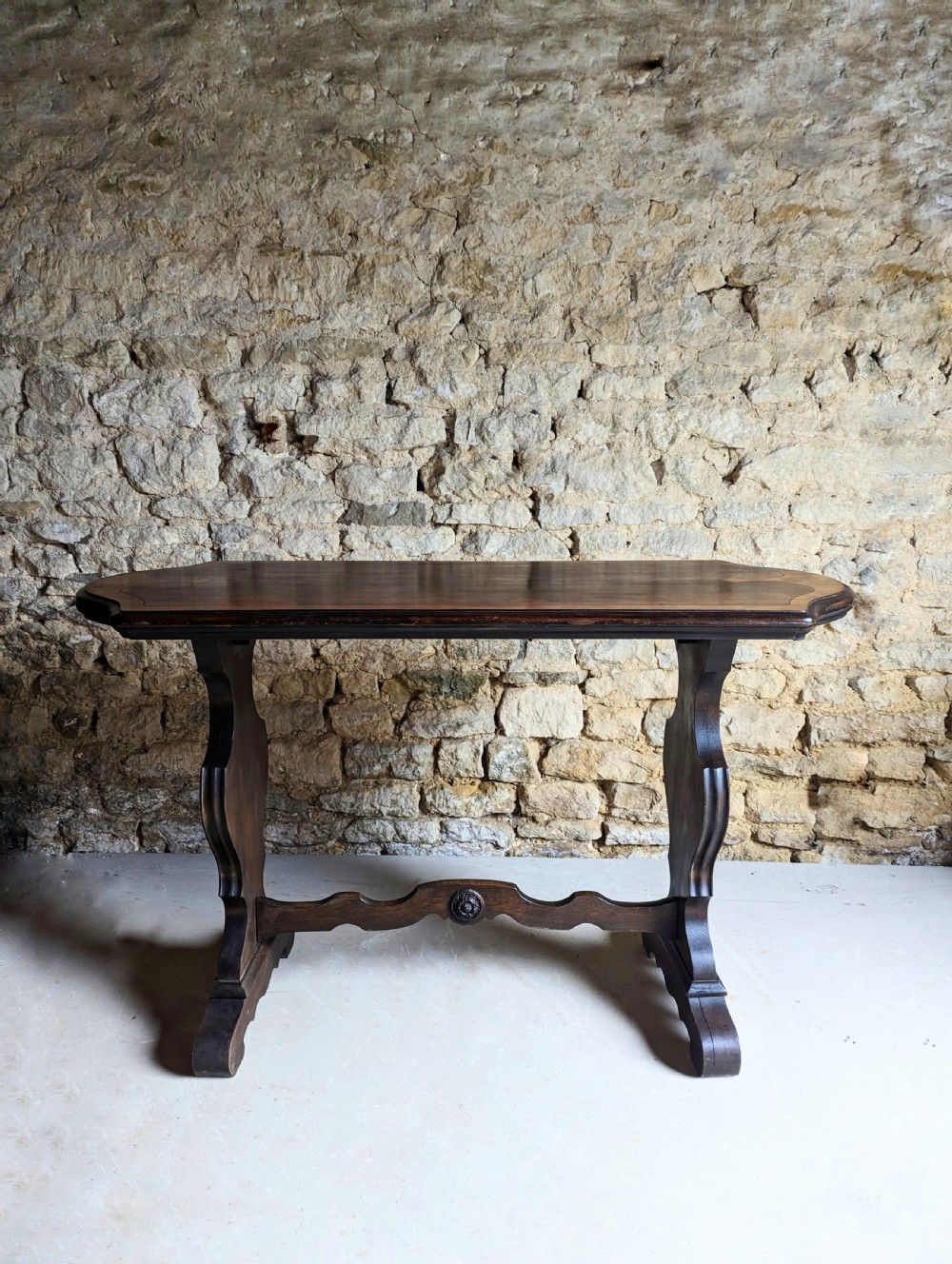 A late 19th-century dark oak trestle table featuring a shaped top with contrasting inlaid border and a low stretcher with a central carved boss. View XI