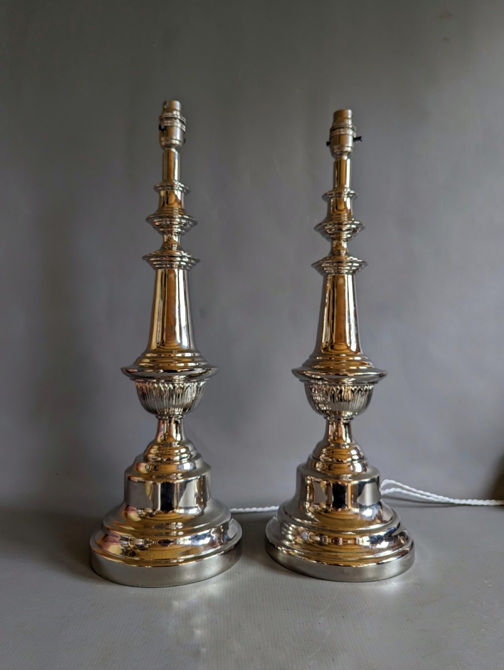 A pair of polished silver-toned metal table lamp bases featuring stepped circular bases and turned baluster columns.