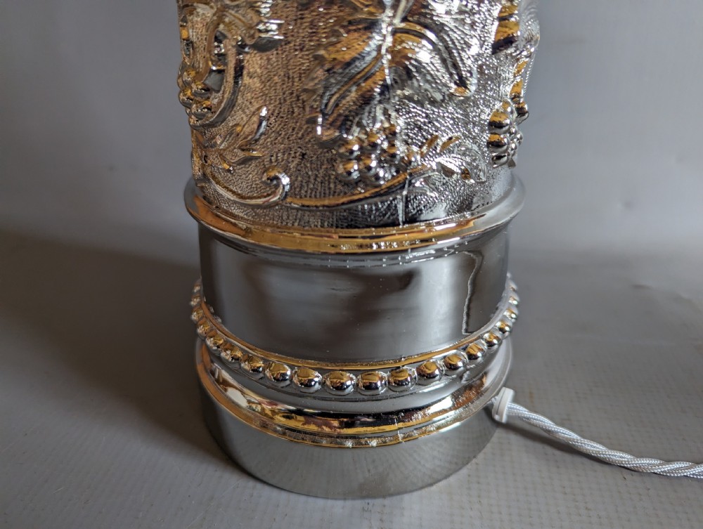 A pair of reflective nickel-plated table lamps featuring embossed foliate relief, scroll handles, and beaded rim details. View VI