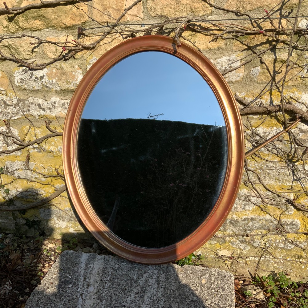An antique oval wall mirror featuring a moulded gilt frame and reflective glass plate.