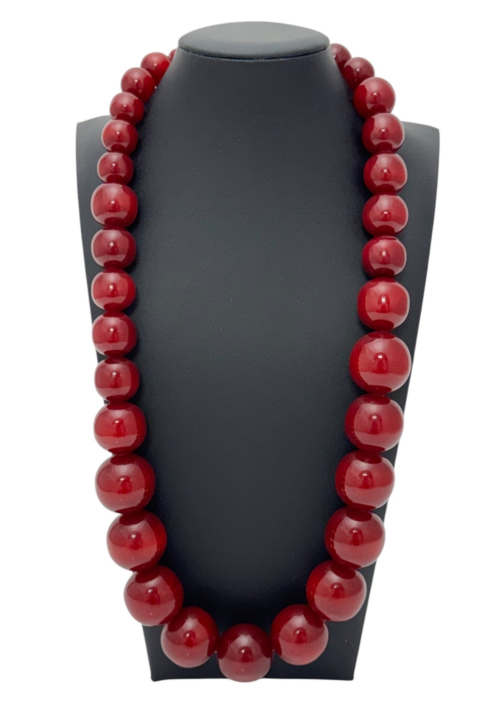 A graduated strand of translucent deep cherry red spherical beads displayed on a dark grey jewelry bust.