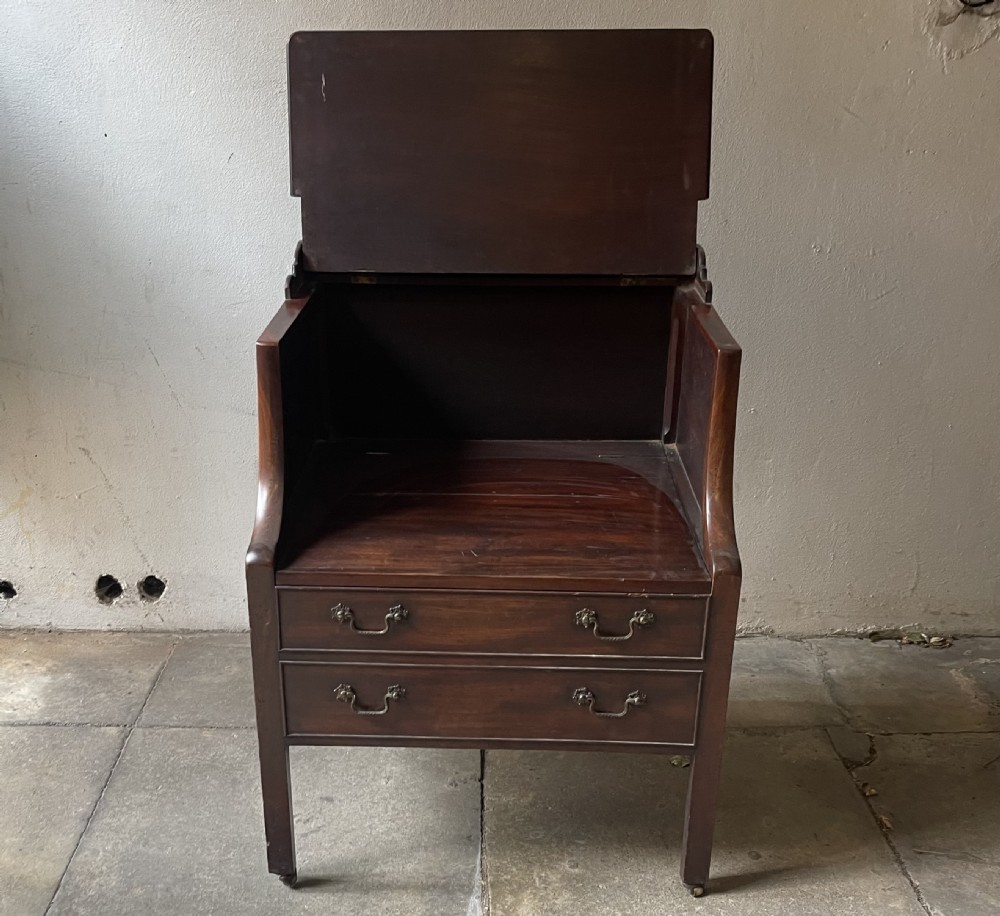A George III dark mahogany bedside commode featuring an open upper shelf, a shaped tray top, two lower drawers with brass handles, and square legs on small brass castors. View III