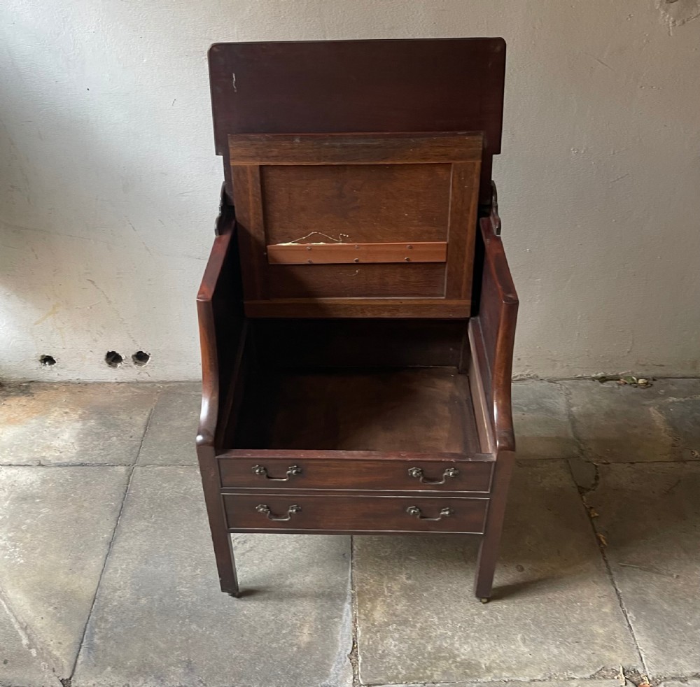 A George III dark mahogany bedside commode featuring an open upper shelf, a shaped tray top, two lower drawers with brass handles, and square legs on small brass castors. View IV