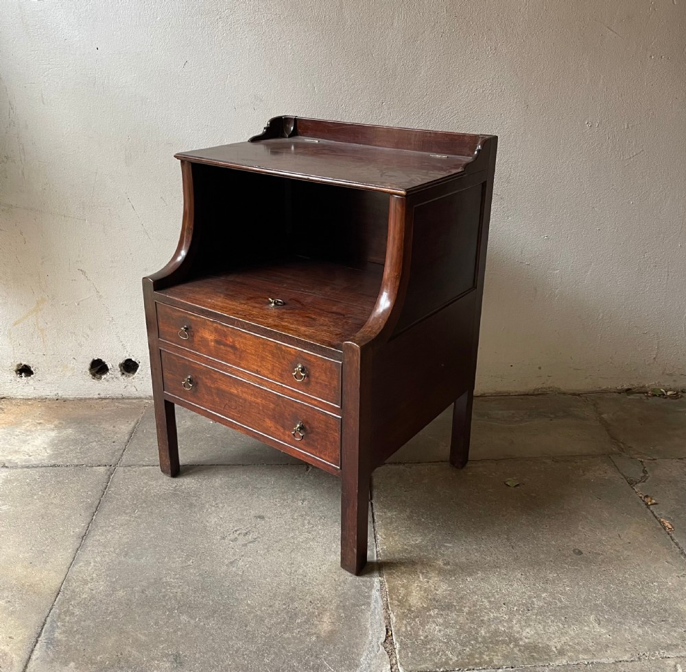 A George III mahogany bedside commode featuring an upper open compartment, gallery top, and lower drawers with brass handles.