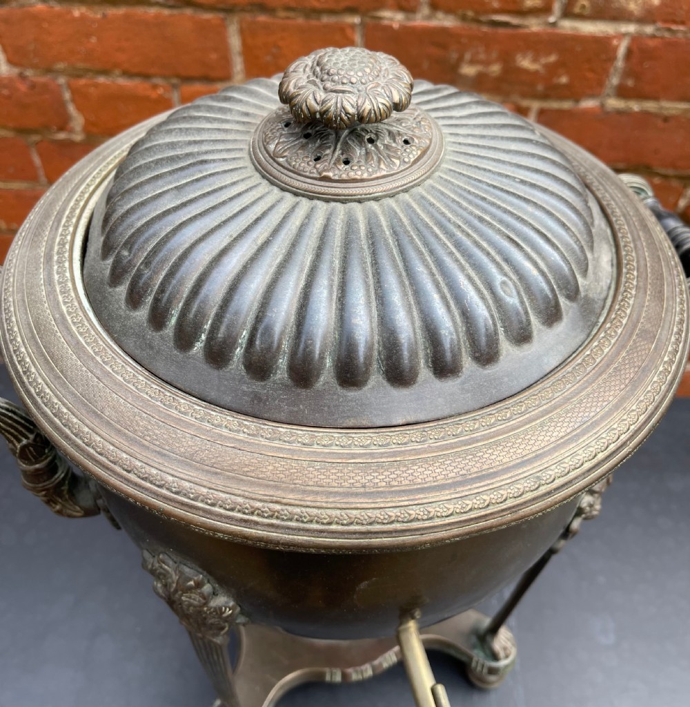 An antique Regency patinated metal tea urn featuring a fluted lid, twin scroll handles, a front brass spigot, and reeded legs resting on a shaped base. View III