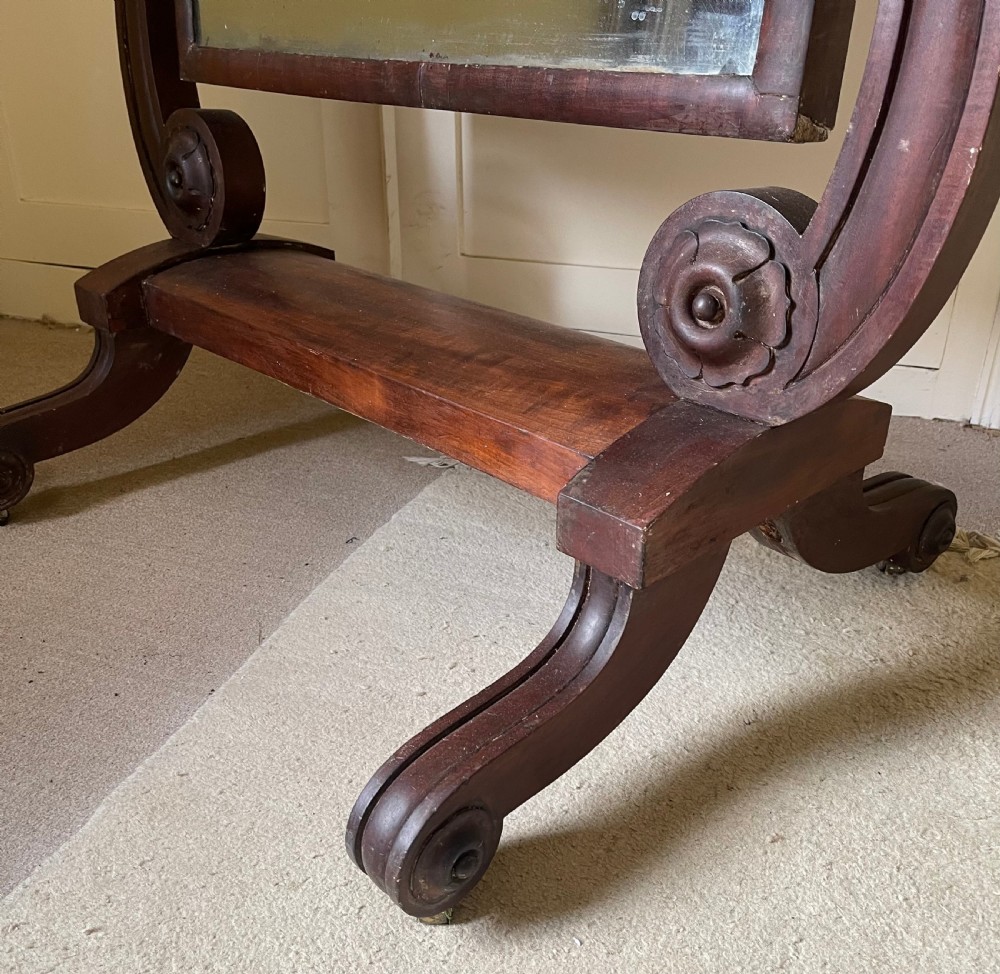 A William IV mahogany cheval mirror featuring a rectangular swivelling frame set between carved scroll upright supports on a trestle base. View II