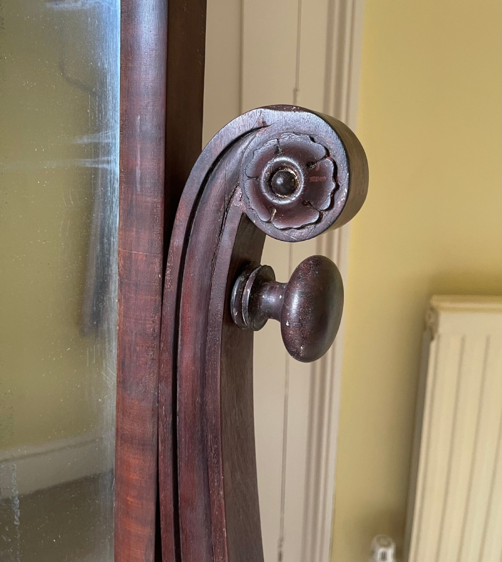 A William IV mahogany cheval mirror featuring a rectangular swivelling frame set between carved scroll upright supports on a trestle base. View III