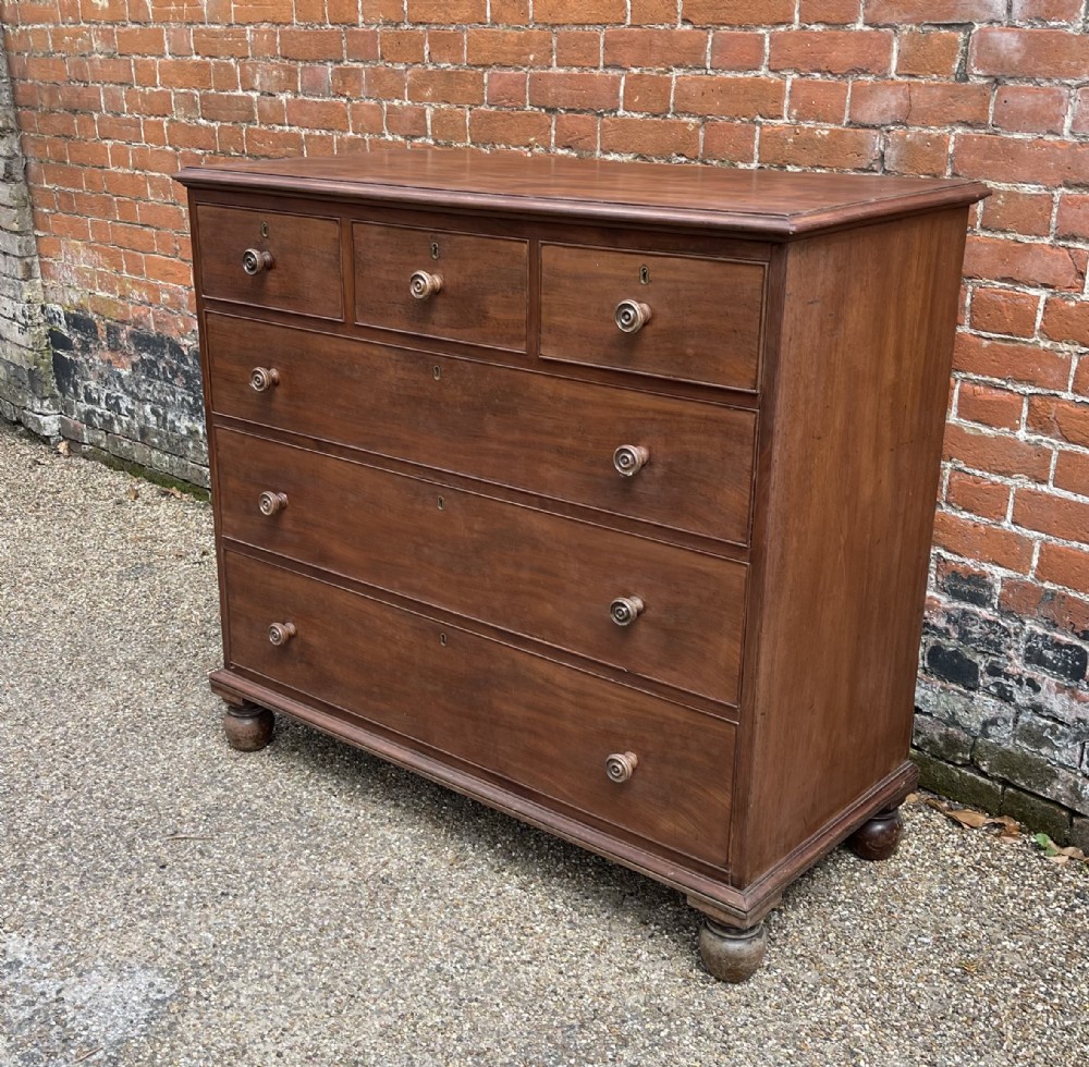 An antique mahogany chest of drawers featuring three short drawers over three long graduated drawers with turned wooden knobs and bun feet.