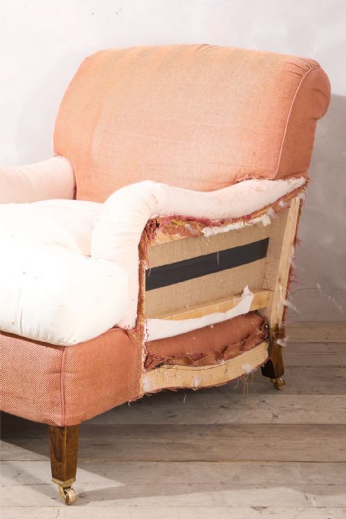 fig 1. A large twentieth-century armchair covered in terracotta-coloured lining fabric with scrolled arms, deep seat cushion, and square tapered wooden legs on brass castors.