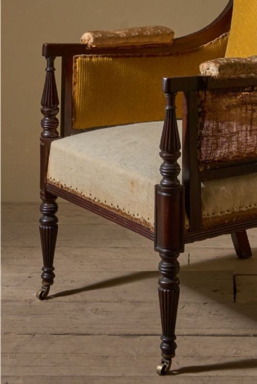fig 1. A 19th century mahogany library chair featuring reeded arms and legs, brass castors, exposed hessian sides, and yellow corduroy cushion fabric.