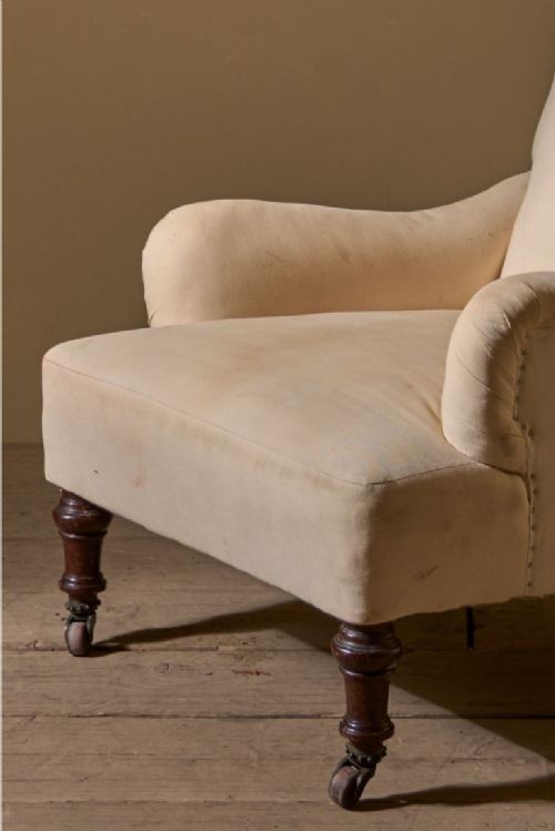 fig 1. A 19th-century Bridgewater-style armchair upholstered in light cream fabric with turned mahogany front legs on castors.