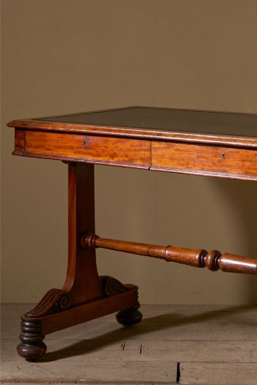 fig 1. An Early Victorian mahogany writing table featuring a dark leather inset top, two frieze drawers, and trestle end supports linked by a turned stretcher.