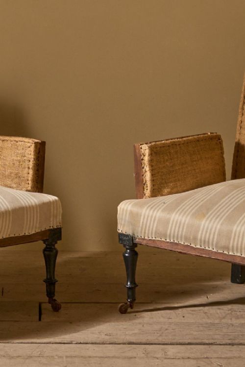 fig 1. A pair of 19th-century French Napoleon III armchairs with square sides, neutral striped seat upholstery, and turned front legs on brass castors.