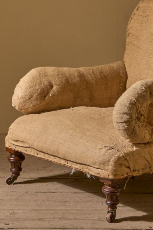 fig 1. A large 19th-century Grafton style armchair stripped to its natural hessian under-upholstery, featuring scroll arms and turned wooden front legs on brass castors.