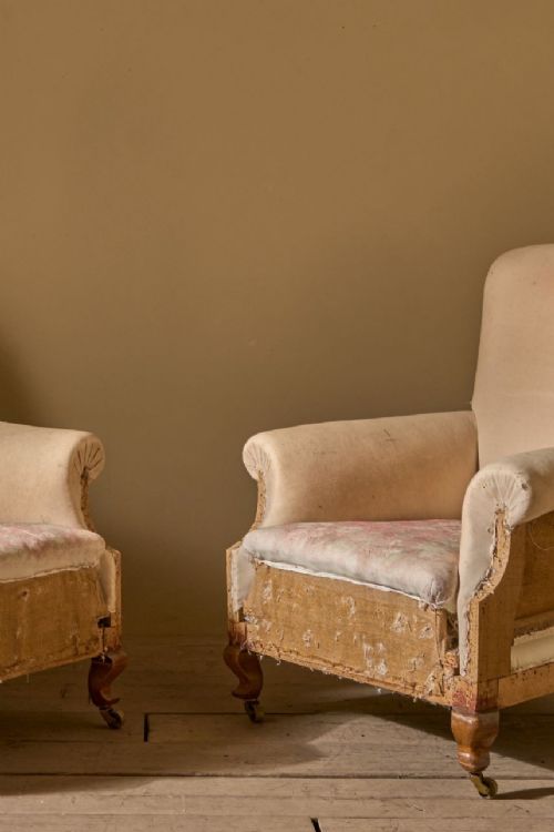 fig 1. Pair of Edwardian scroll back armchairs upholstered in beige calico fabric resting on turned front legs with brass castors.