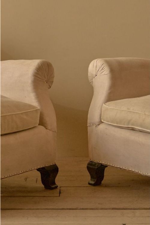 fig 1. A pair of 1920s French club armchairs upholstered in neutral beige calico with exposed hessian lower panels and dark turned wooden feet.