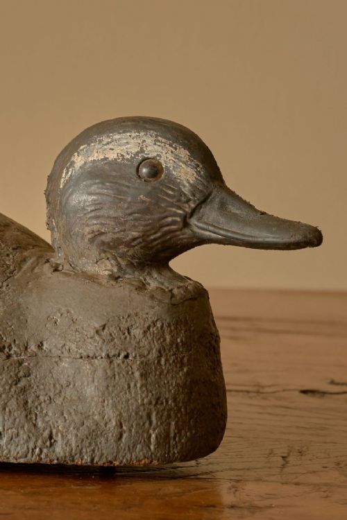 fig 2. A carved wooden decoy duck with a grey painted body, textured finish, and a green painted speculum patch on its side.