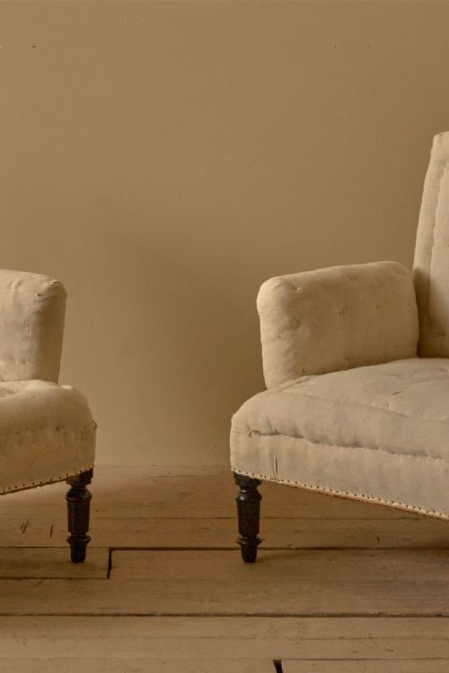 fig 1. A pair of nineteenth-century French Napoleon III high-backed armchairs upholstered in off-white calico with pillow arms and dark turned wooden front legs.