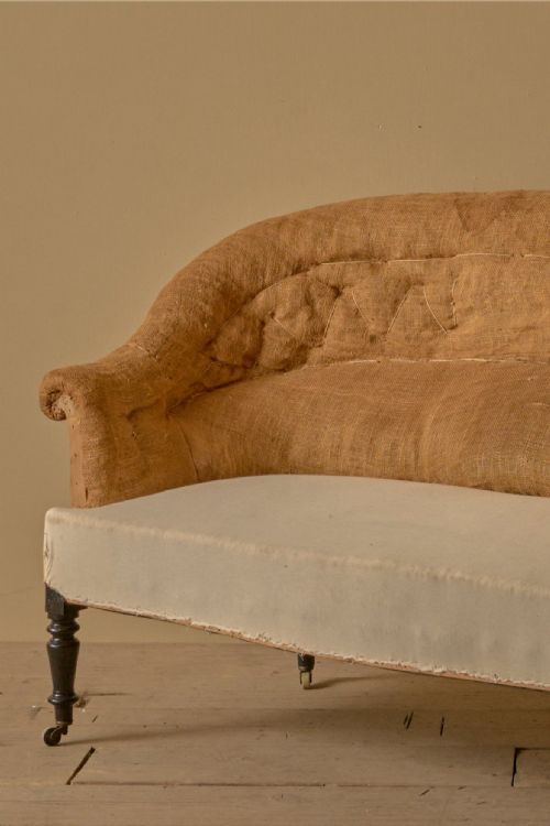 fig 1. A nineteenth-century French Napoleon III sofa with a curved back, hessian covering, and turned dark timber legs on castors.