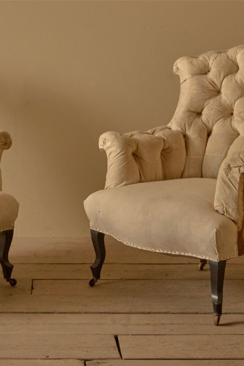 fig 1. A pair of French 19th-century Napoleon III high-back armchairs upholstered in cream fabric with deep buttoning and dark legs on castors.
