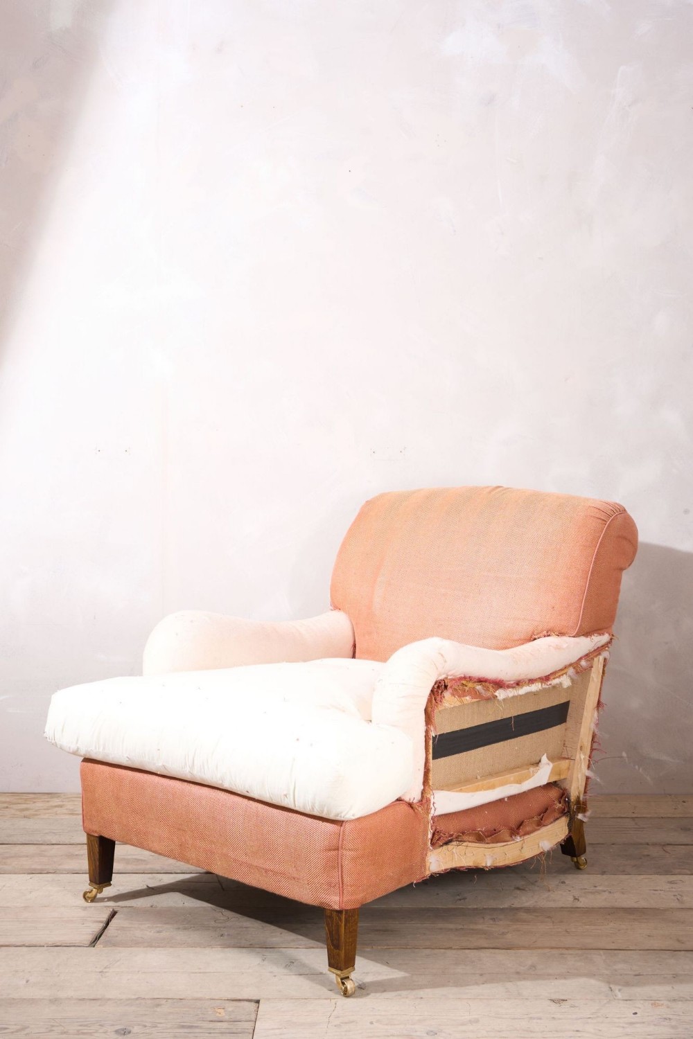 A large twentieth-century armchair covered in terracotta-coloured lining fabric with scrolled arms, deep seat cushion, and square tapered wooden legs on brass castors.